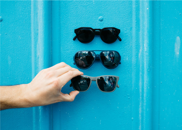 Distil Union MagLock Sunglasses are held in place on a blue metal wall thanks to hidden magnets in the frames